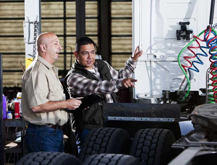 A CDL trainer and and trucking student looking over a commercial truck.