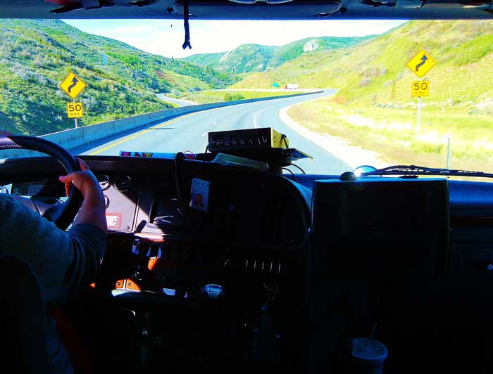 A commercial truck driver in the cab of his truck driving down a country road.