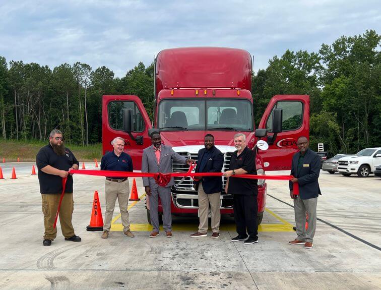 Image distinguished guests and campus president Brad Barber in front of a GDA truck cutting a red ribbon.