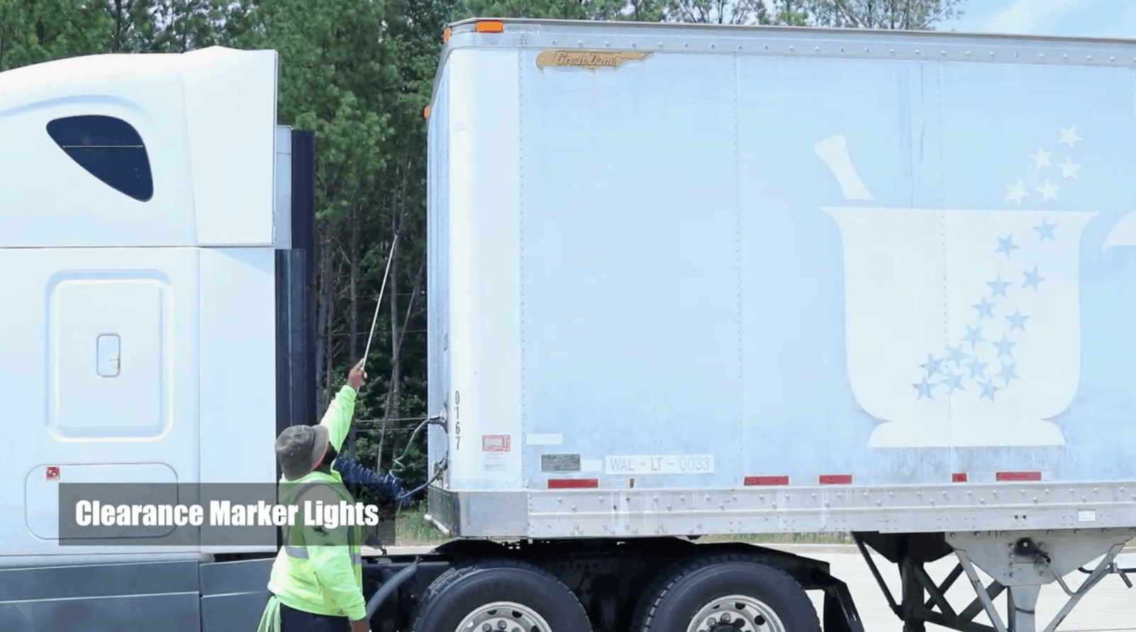 CDL instructor pointing to clearance marker lights at the top of the semi truck trailer with stick