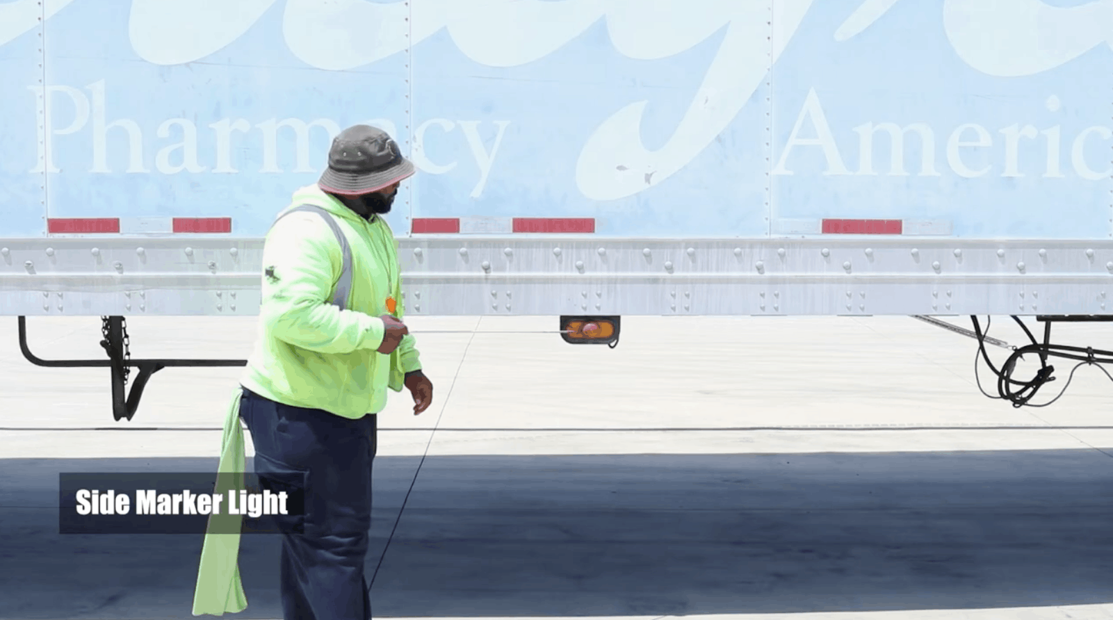CDL instructor pointing at the semi truck's side marker light with a stick