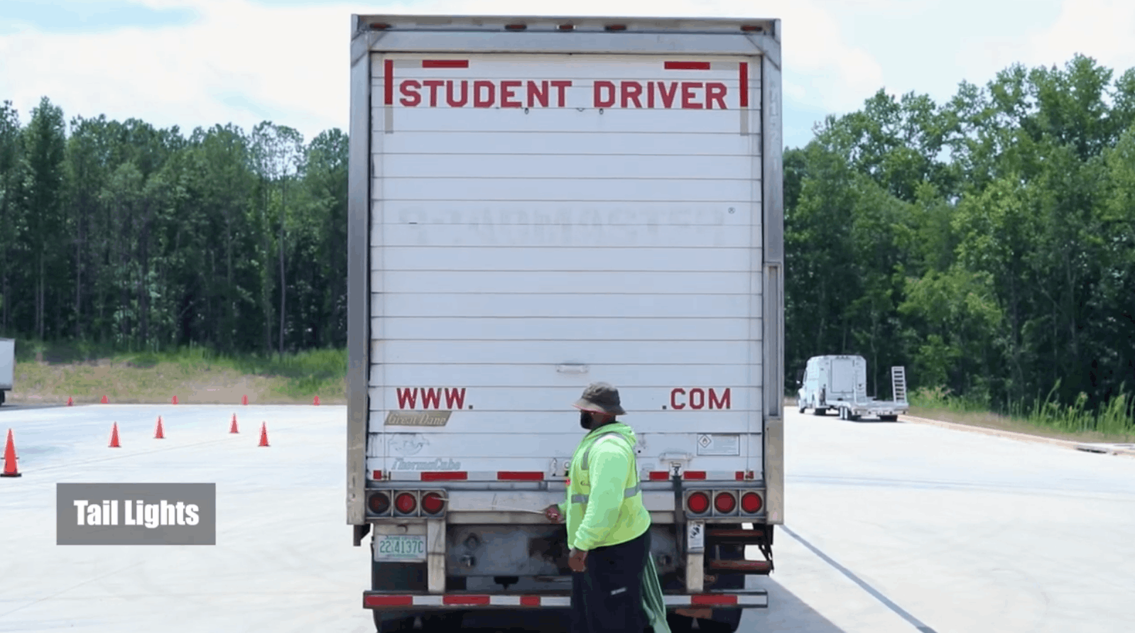 CDL instructor standing at rear of semi truck, pointing at tail lights with a stick