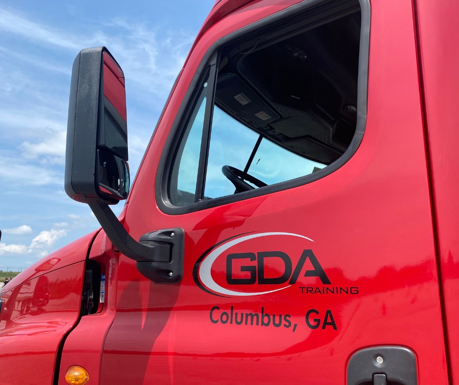 Close-up of the driver's side door of a red semi-truck marked "GDA Training, Columbus, GA" under a blue sky.
